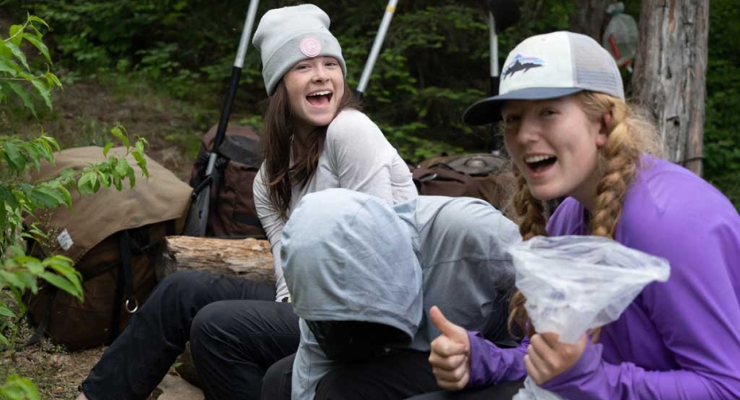 Two students smile excitedly at the camera. Paddles are visible in the background. 